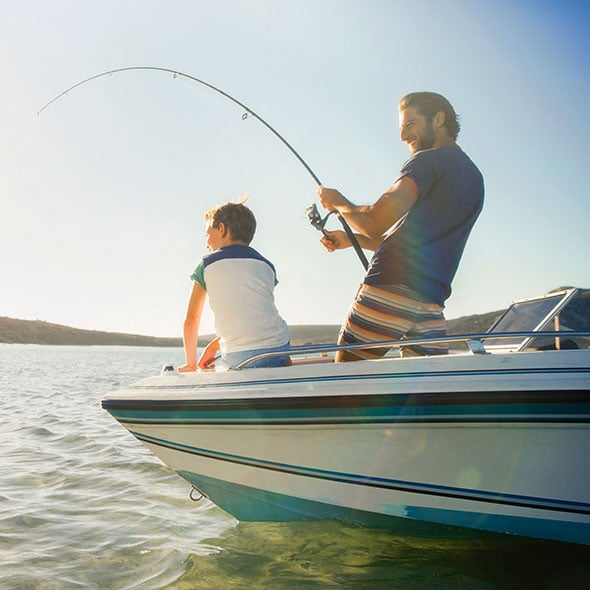 Father and son on boat fishing together on new boat his father purchased with a boat loan from PCU.