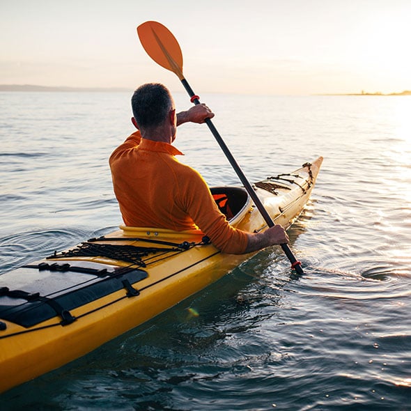 Man kayaking on vacation after reaching his savings goals with a PCU savings account