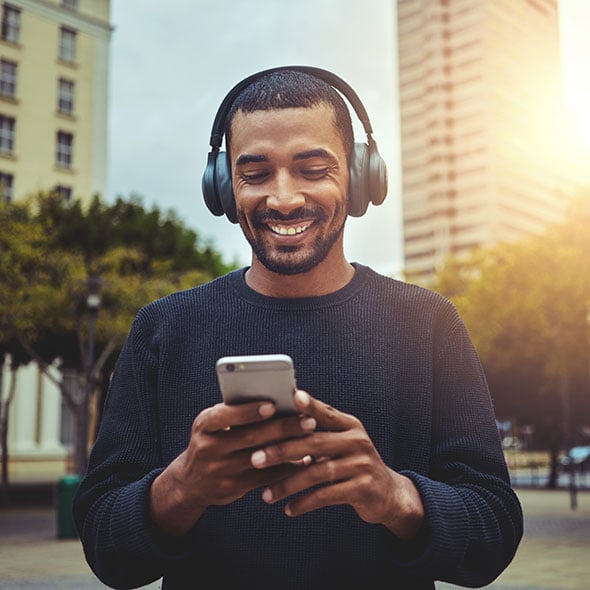 Man walking through the city, looking at his mobile checking account with PCU credit union.
